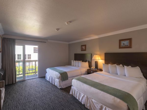 A hotel room with two double beds, nightstand, lamps, dresser, and a balcony door with curtains.