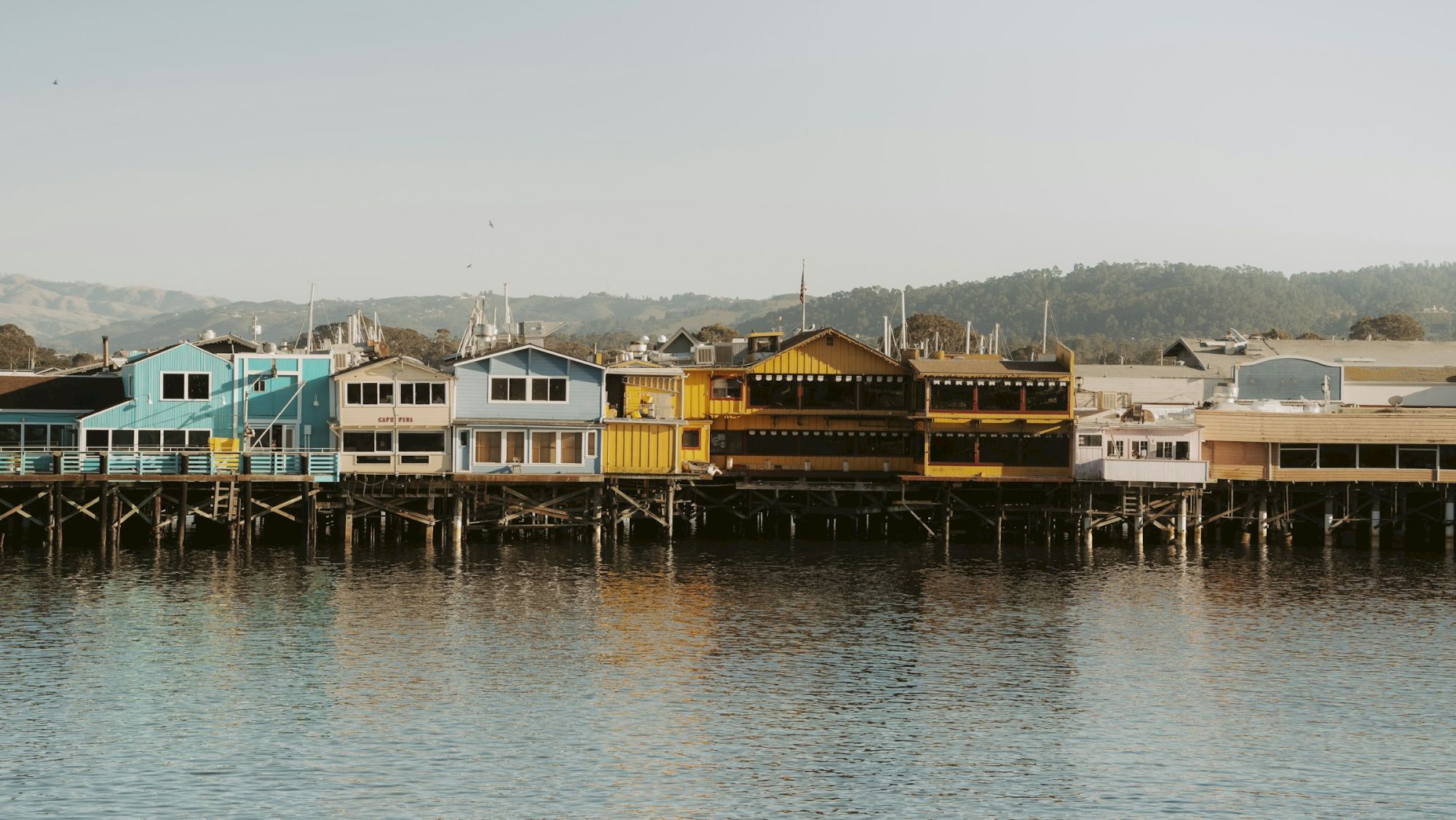 Colorful houses on stilts along a calm waterfront, reflecting a seaside row of bright, pastel shacks.