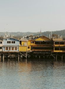 A row of colorful waterfront houses lined along calm water with boats docked in front, likely a seaside village.